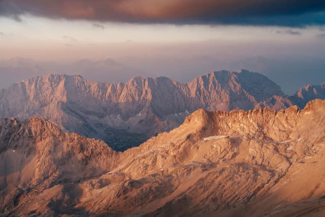 Sunlit mountain ridges glowing in warm evening light beneath a dramatic cloudy sky