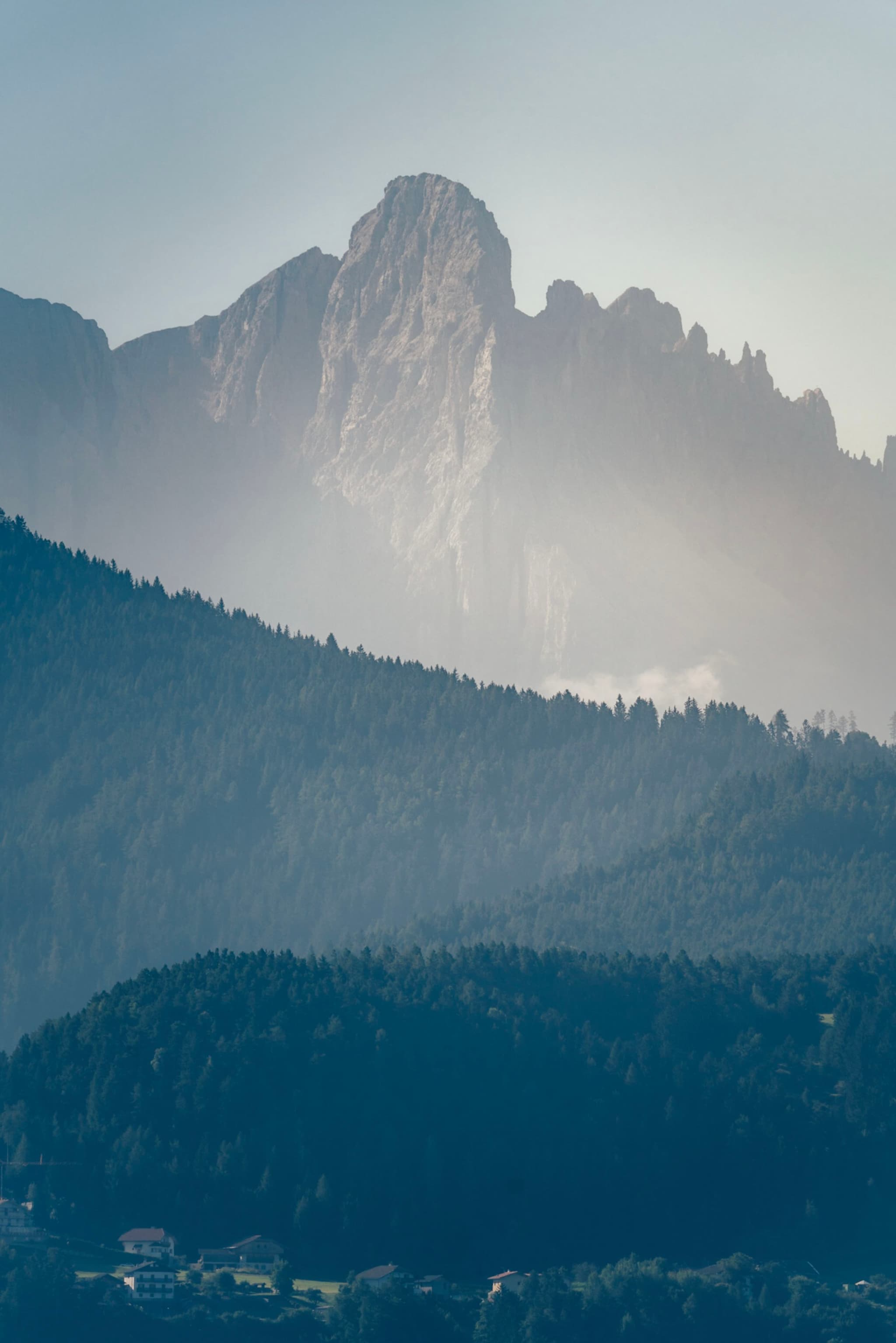 A misty mountain landscape with layered hills and a prominent rocky peak in the background