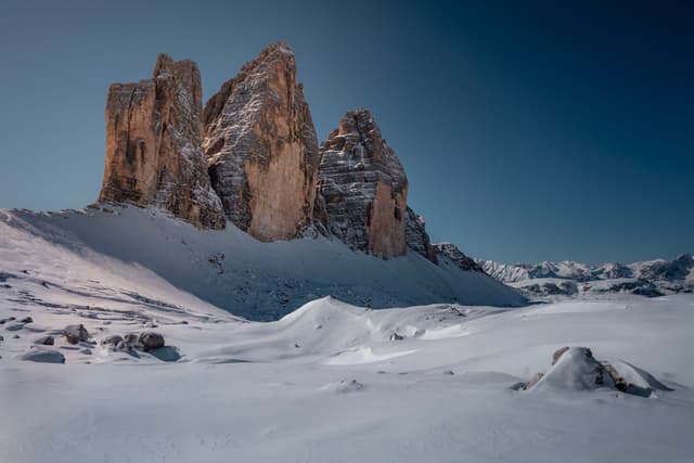 Jagged rocky peaks rise above a vast snow-covered landscape under a clear blue sky
