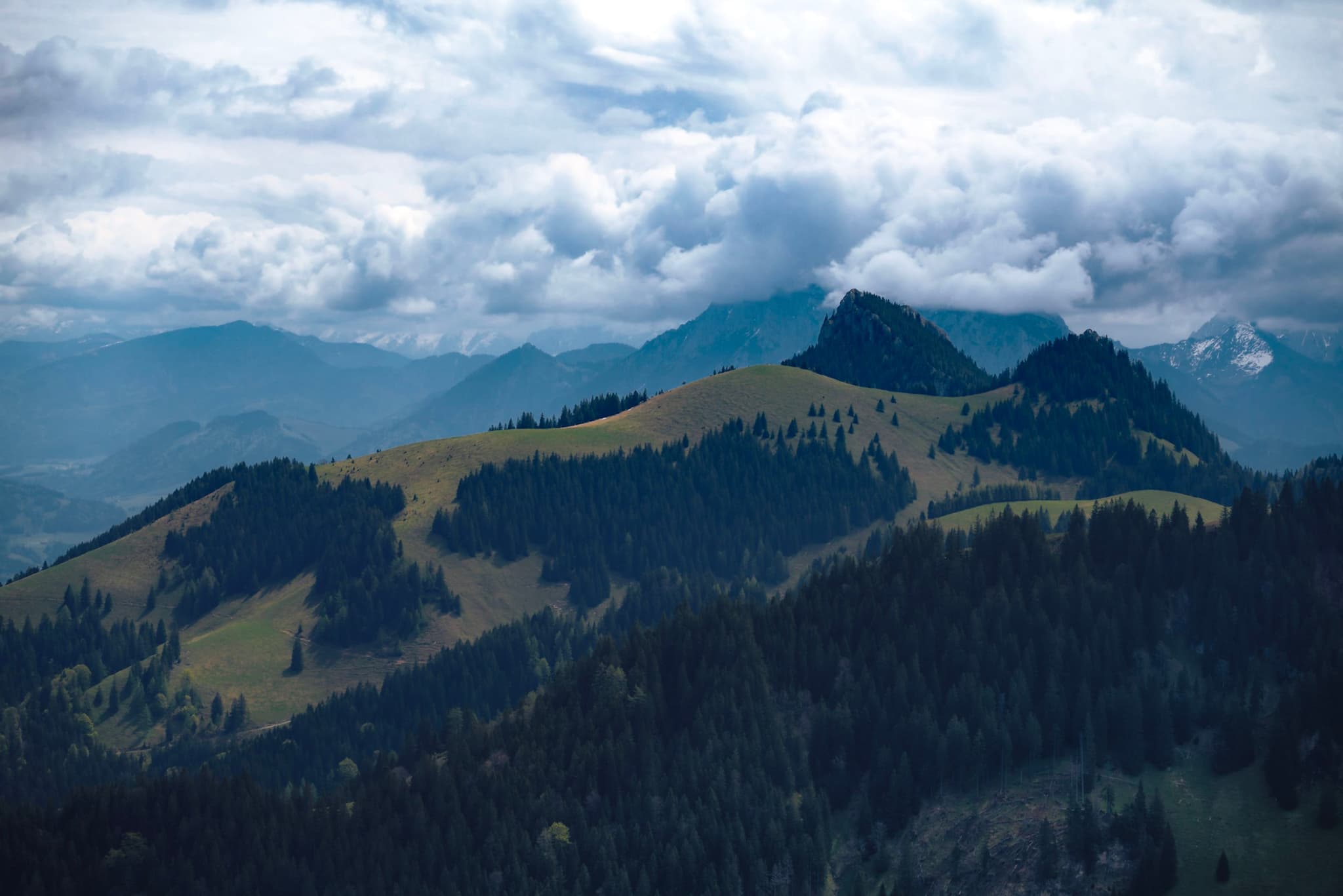 Layered forested mountains with open grassy ridges under thick, dramatic cloud cover