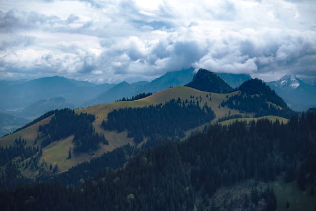 Layered forested mountains with open grassy ridges under thick, dramatic cloud cover