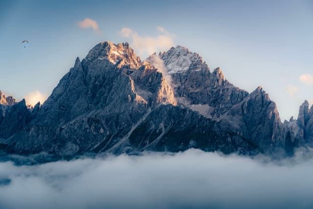 A majestic mountain range with rugged peaks, partially shrouded in clouds, under a clear blue sky