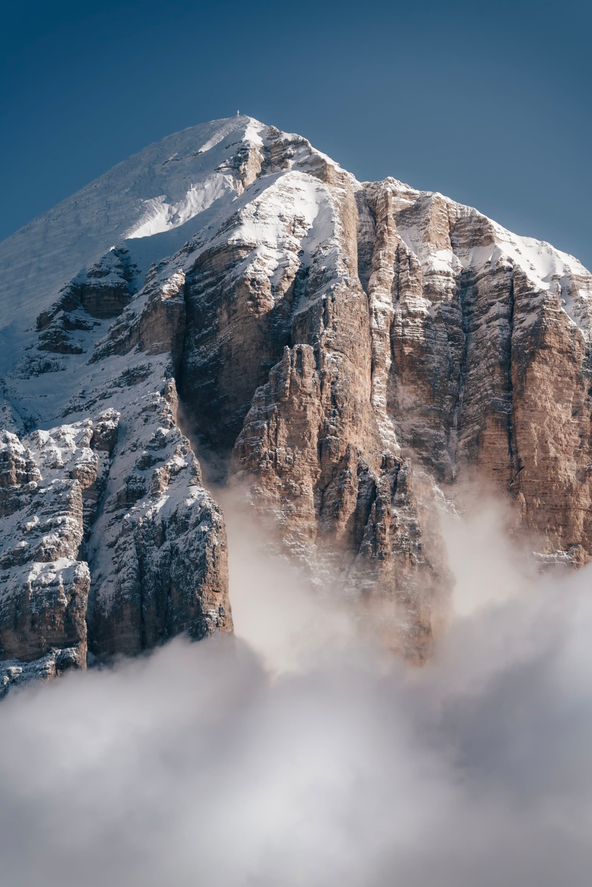 A majestic snow-capped mountain peak rising above clouds under a clear blue sky