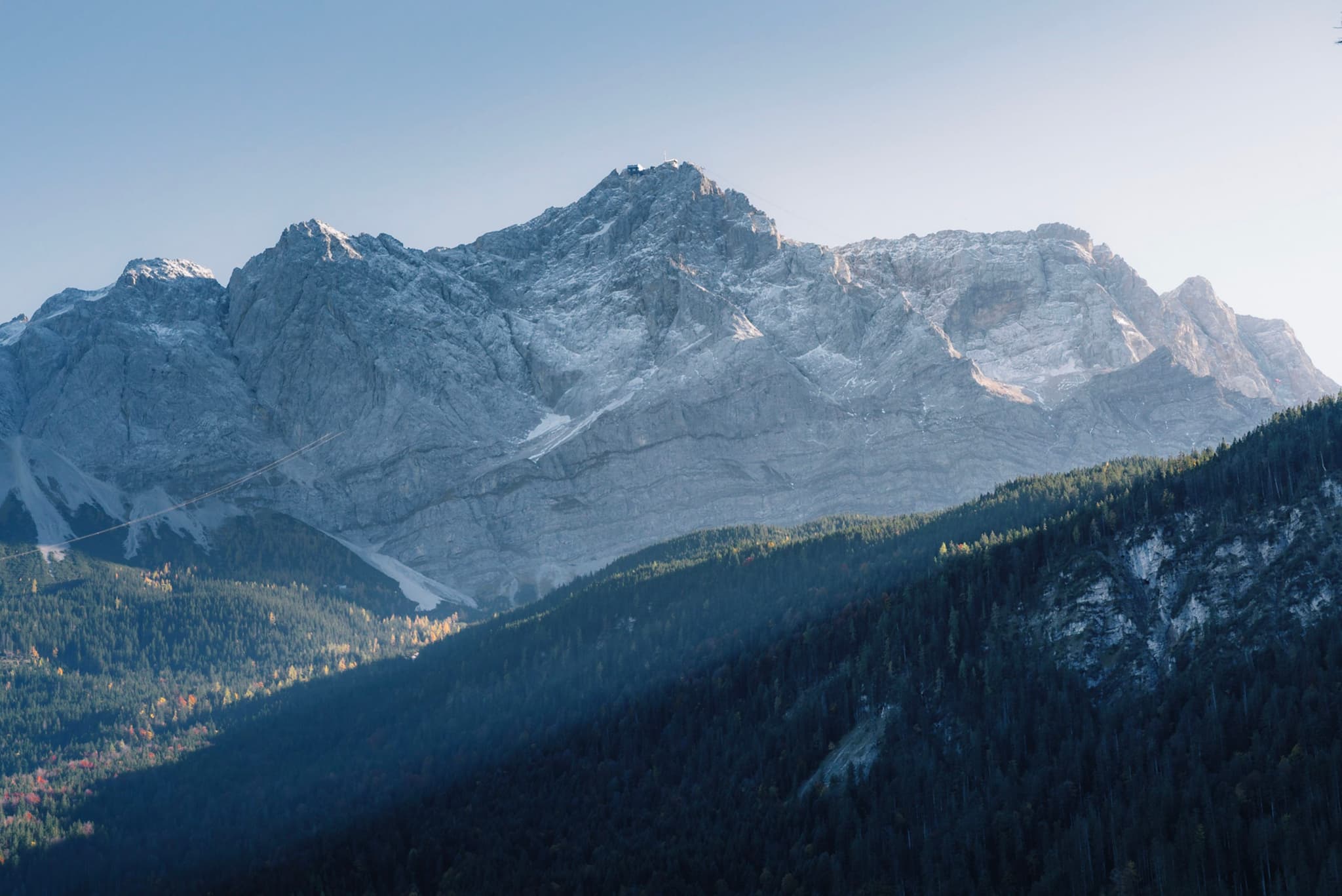 A majestic mountain range with snow-capped peaks and a forested valley below, under a clear blue sky