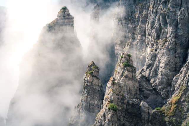 Jagged mountain peaks partially shrouded in mist, with rugged rock formations and patches of greenery