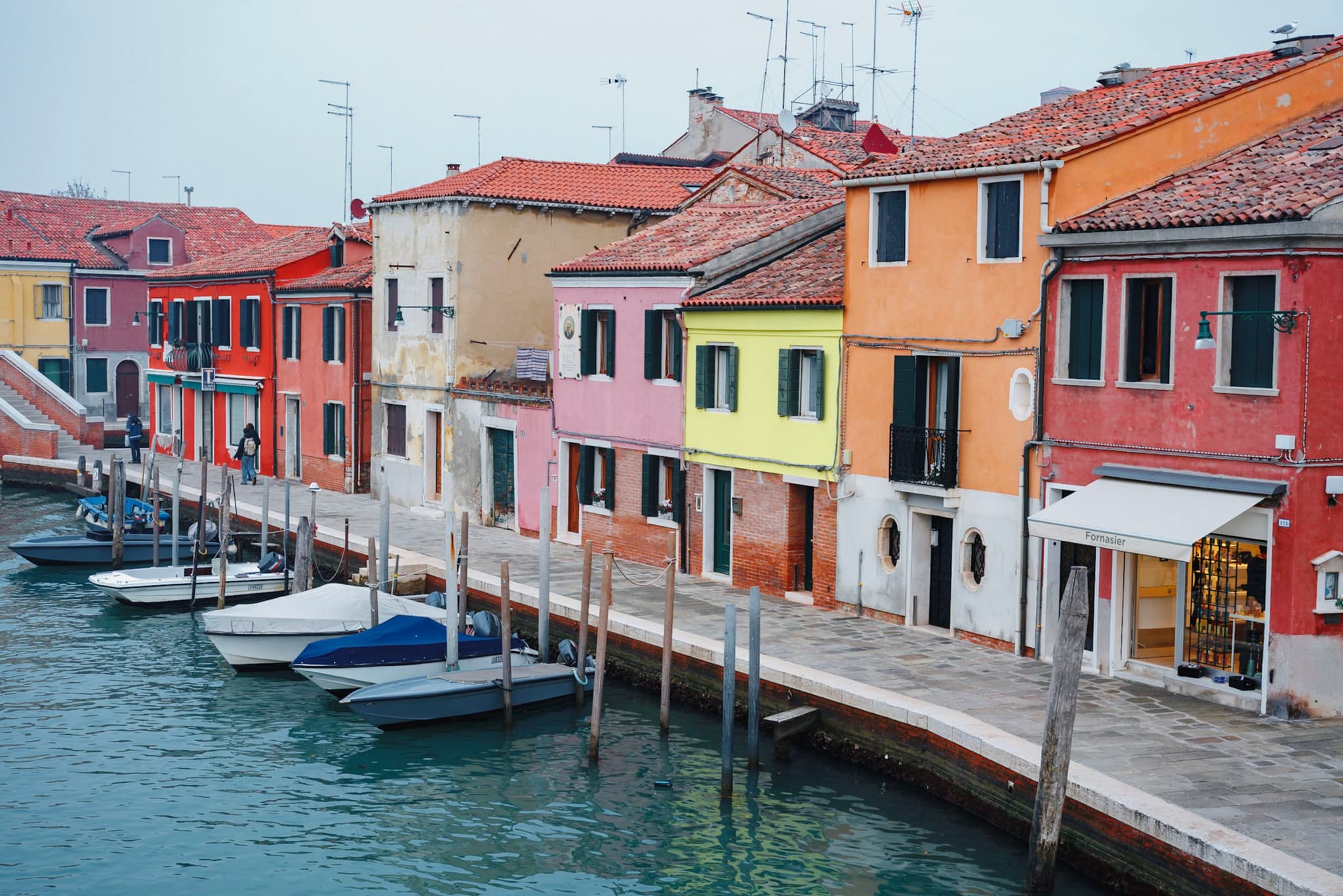 Colorful houses line a canal with small boats moored along the water's edge