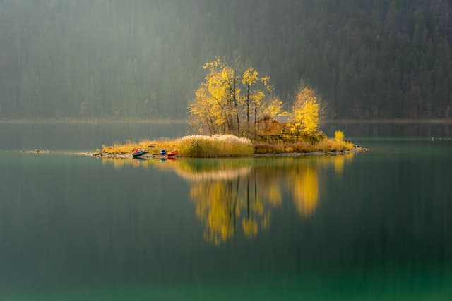Tiny autumn island with golden trees reflected in the calm, misty lake