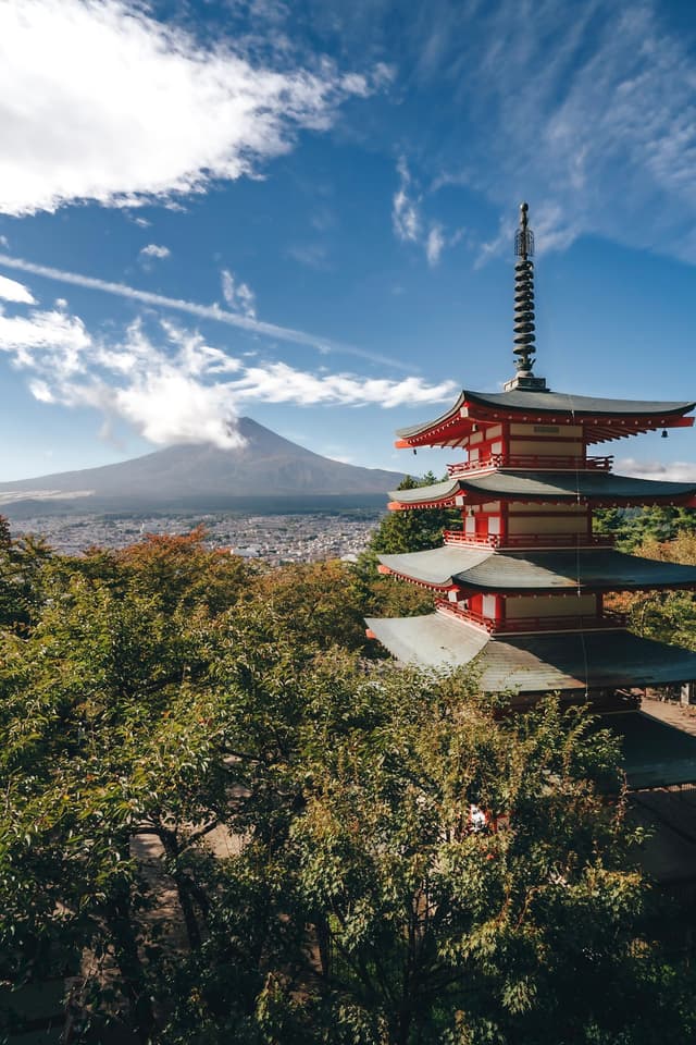 red pagoda rising above autumn trees with snow-capped Mount Fuji in the background under a bright blue sky with scattered clouds
