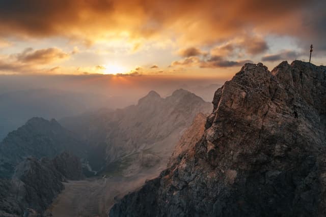 Sunset light breaking through clouds over rugged mountain peaks and a rocky ridge in the foreground
