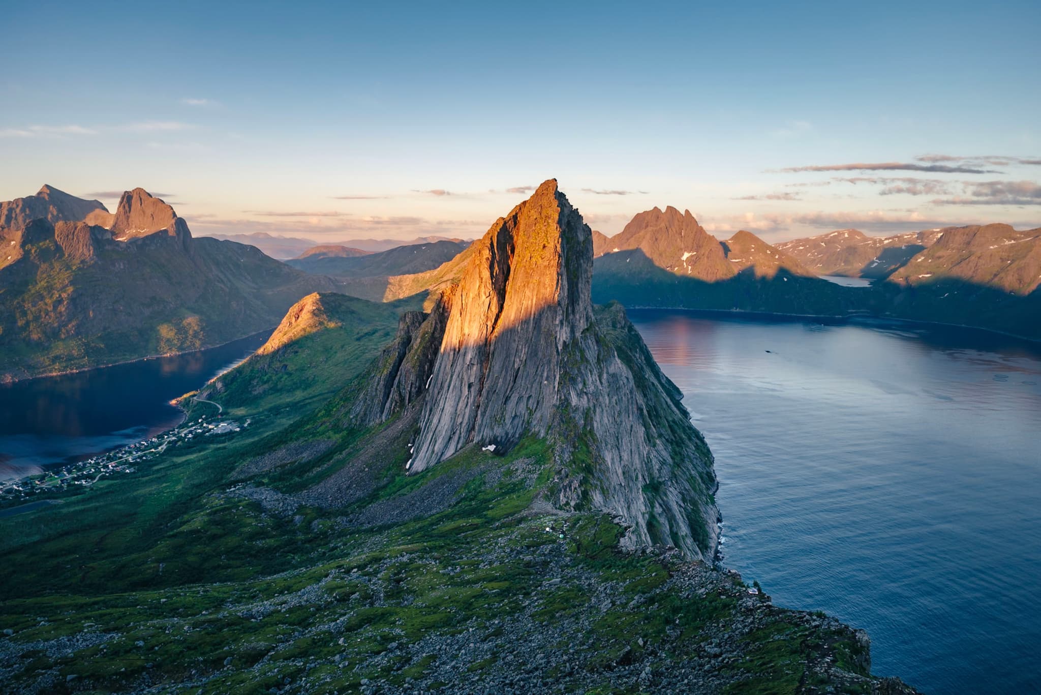 A dramatic mountain peak bathed in warm sunlight, surrounded by a serene body of water and distant mountains under a clear sky