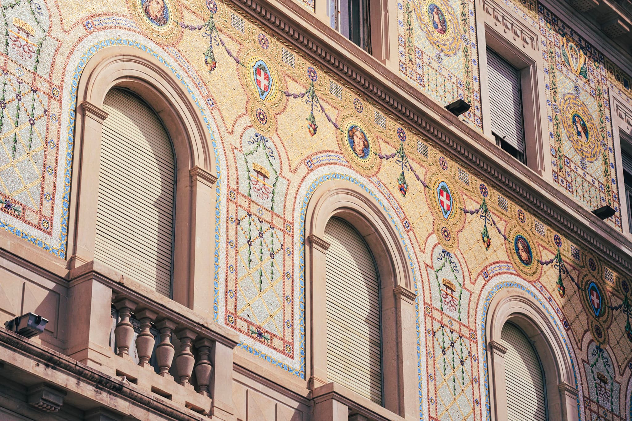 Decoratively painted historic building facade with arched shuttered windows and intricate floral and geometric motifs