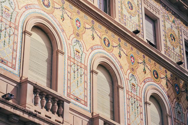 Decoratively painted historic building facade with arched shuttered windows and intricate floral and geometric motifs