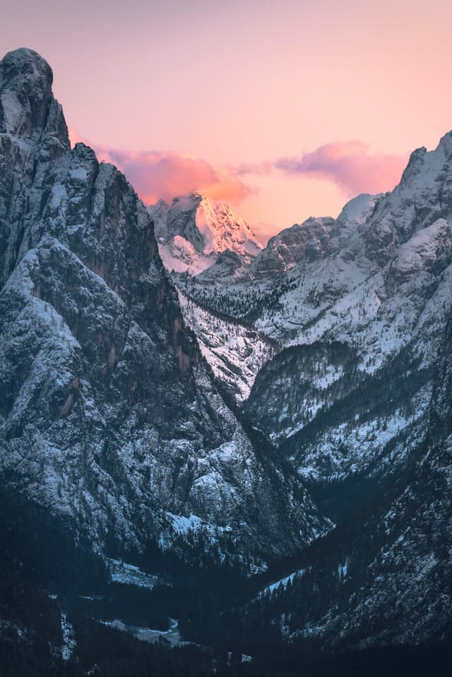 snow-covered mountain valley framed by steep rocky cliffs under a pastel pink and blue sunset sky