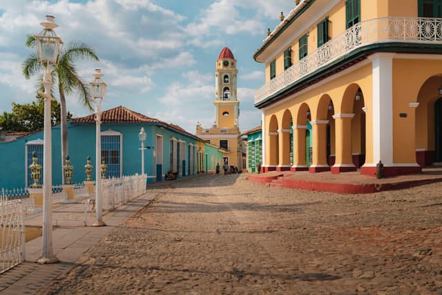 quiet cobblestone courtyard lined with colorful colonial buildings and a distant bell tower under a partly cloudy sky