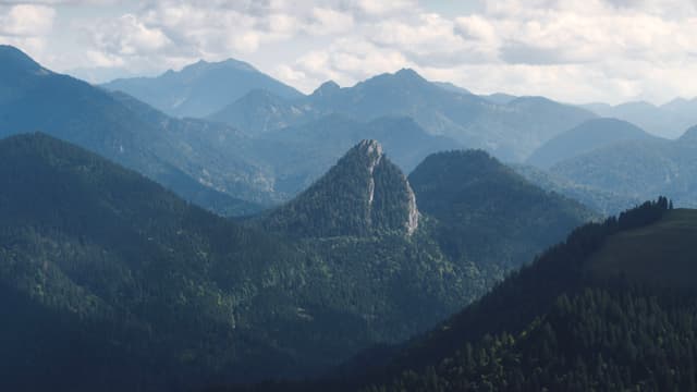 Layered forested mountains fading into the distance under a hazy, cloud-filled sky