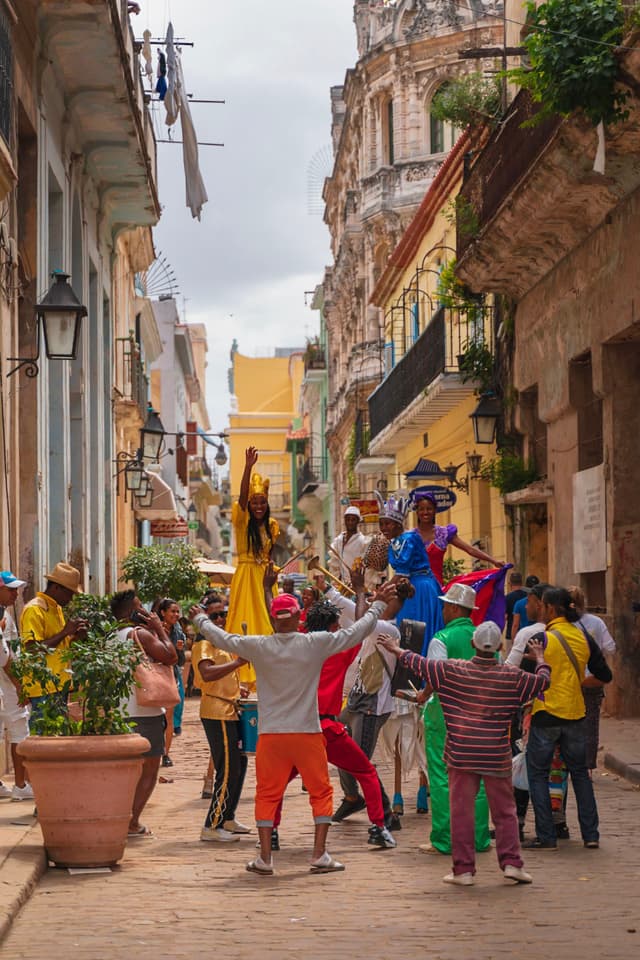 Colorfully dressed performers and residents celebrate together in a narrow historic alleyway lined with old buildings