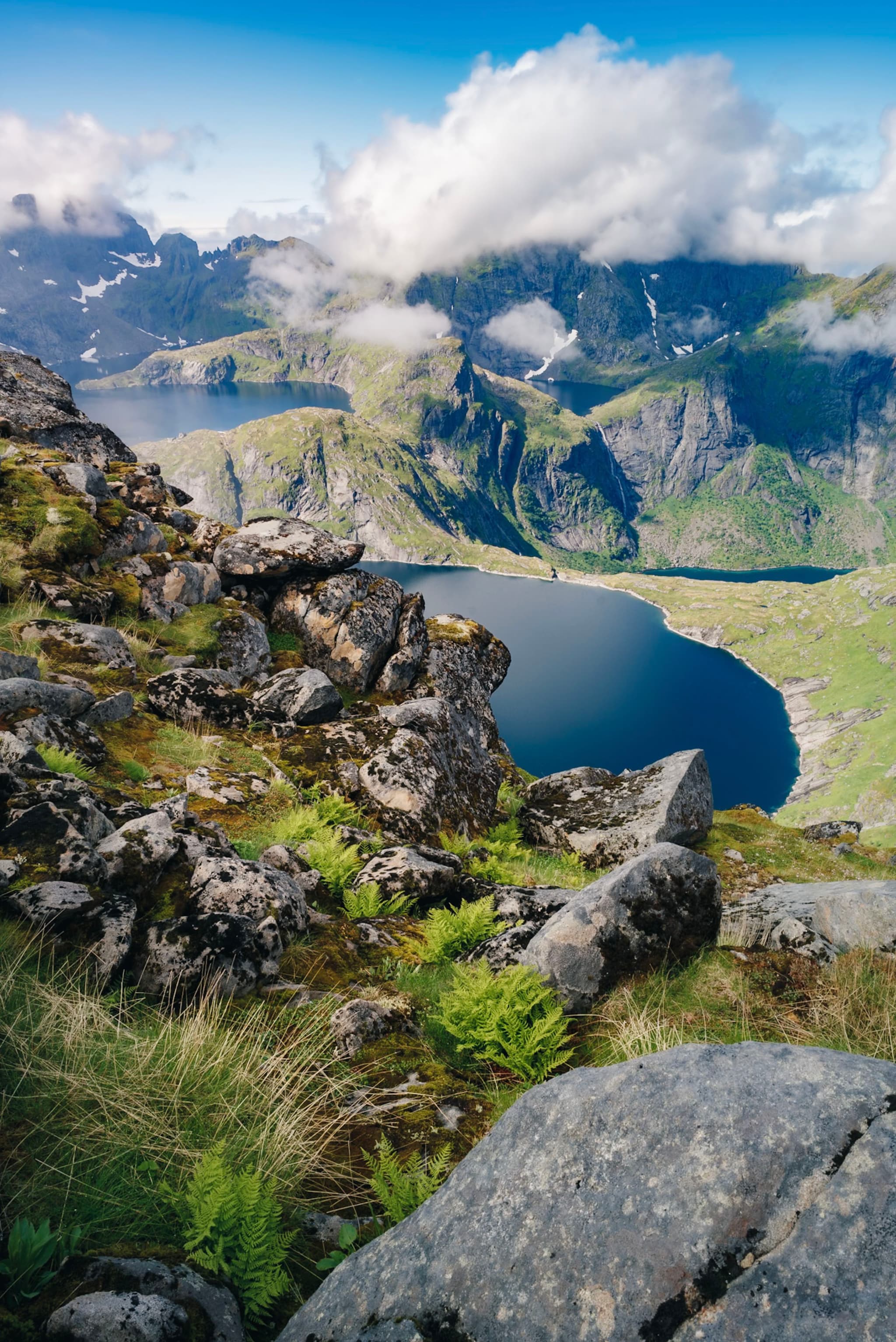 A scenic view of a mountainous landscape with a deep blue lake surrounded by rocky terrain and lush greenery, under a partly cloudy sky