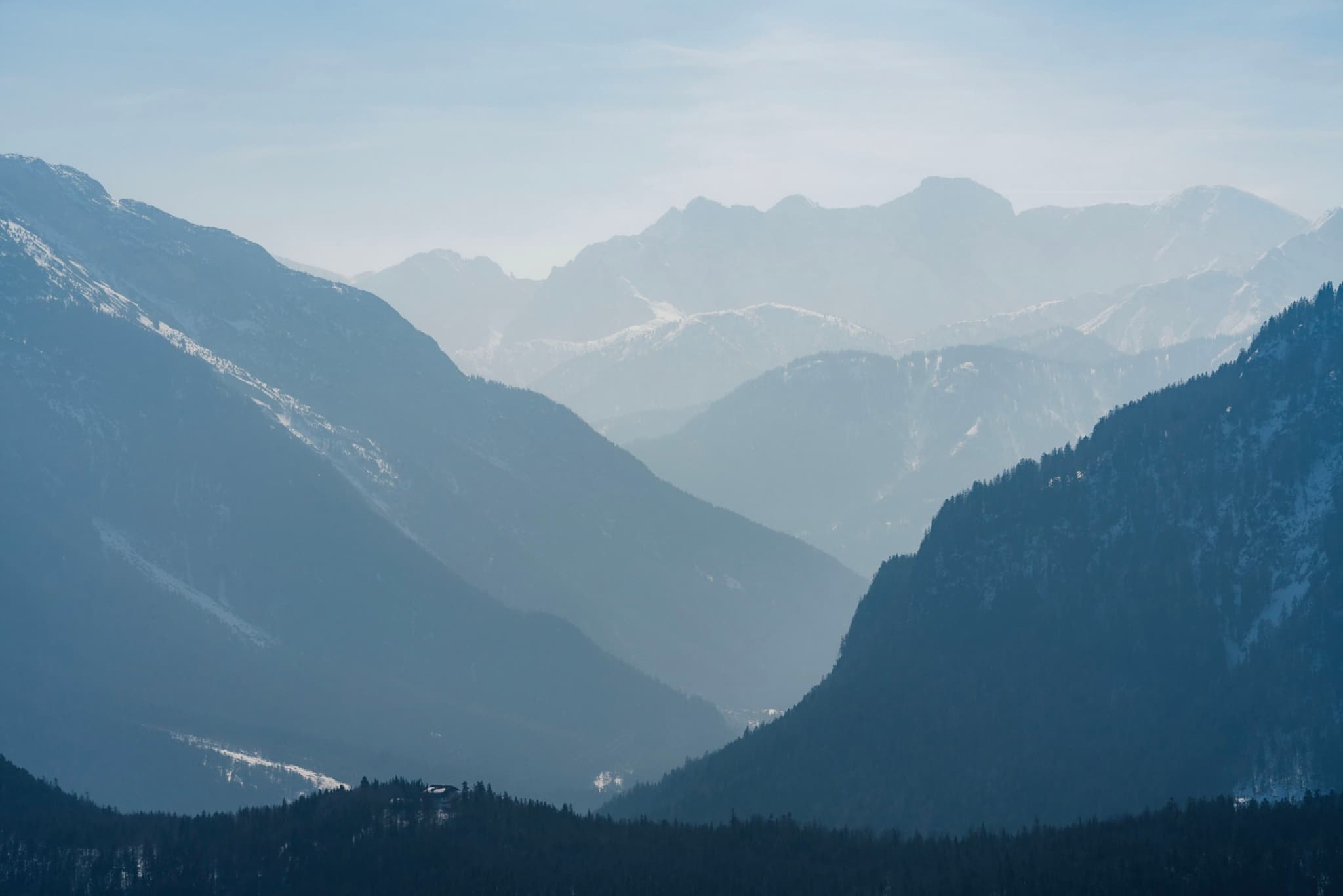 Hazy layered mountain ranges receding into the distance with a deep valley between dark foreground slopes