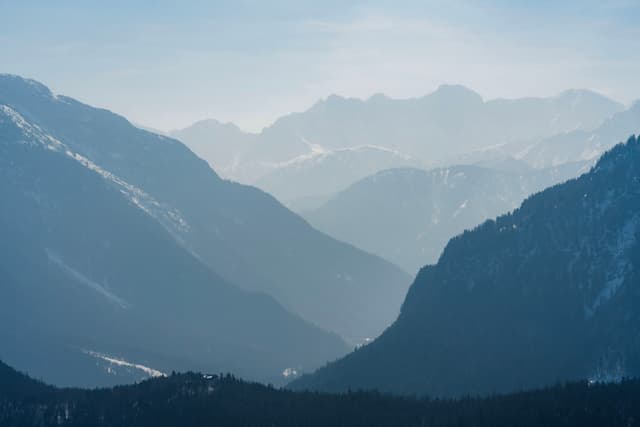 Hazy layered mountain ranges receding into the distance with a deep valley between dark foreground slopes