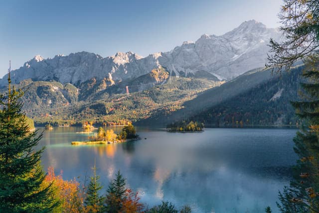 A serene mountain lake surrounded by lush forests and majestic peaks, with sunlight casting gentle rays across the landscape