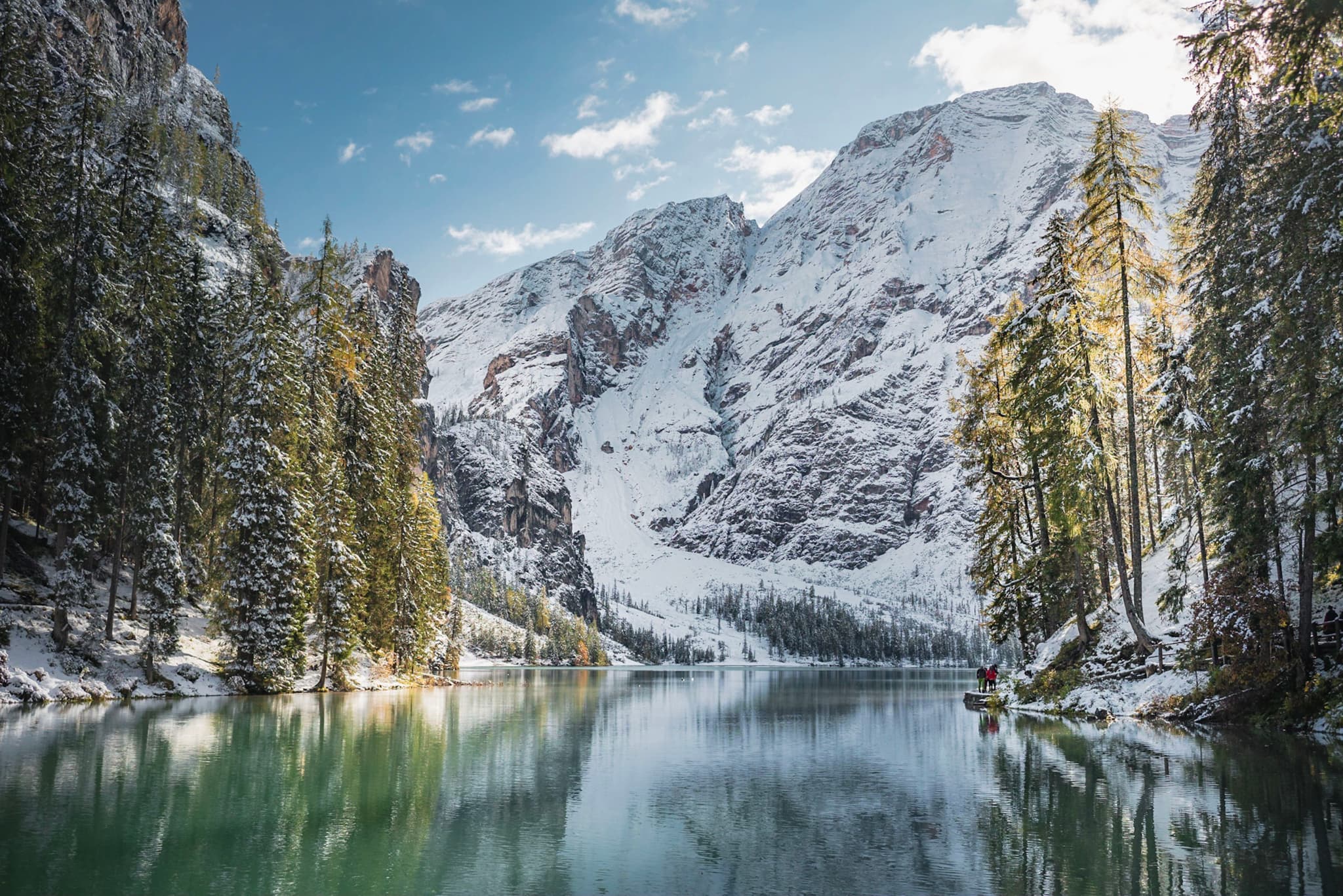 Snow-covered mountains reflecting in a calm alpine lake framed by evergreen trees