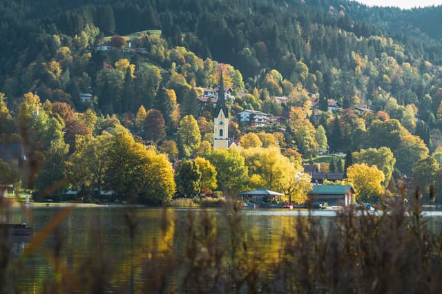 Quiet lakeside village backed by forested hills with a church steeple rising among autumn trees and reflections on the still water