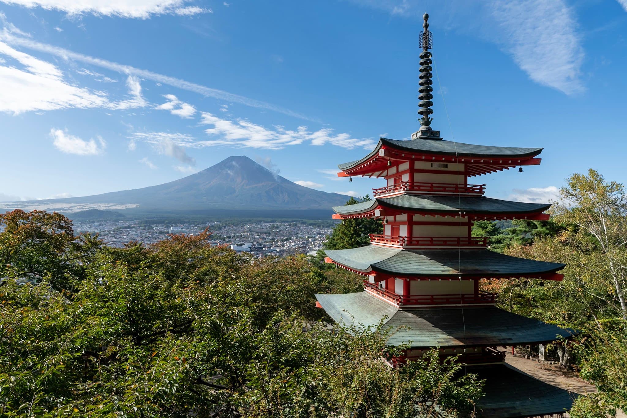 Red pagoda rising above green trees with a snow-capped mountain and clear blue sky in the background
