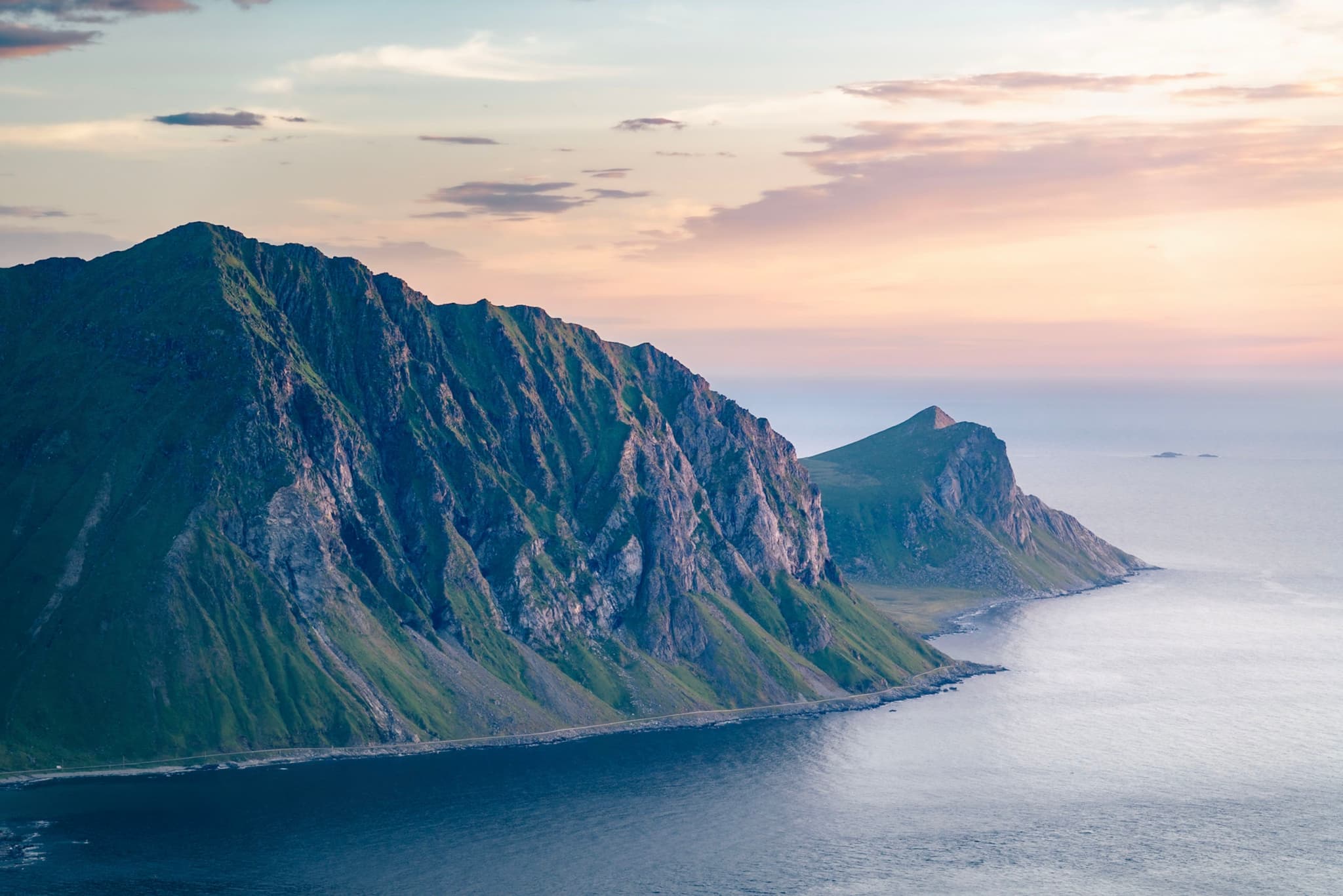 Steep green sea cliffs dropping into calm blue water under a pastel sunset sky