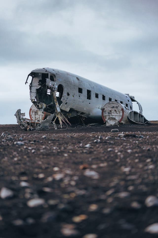 A weathered, abandoned airplane fuselage rests on a desolate, rocky landscape under a cloudy sky