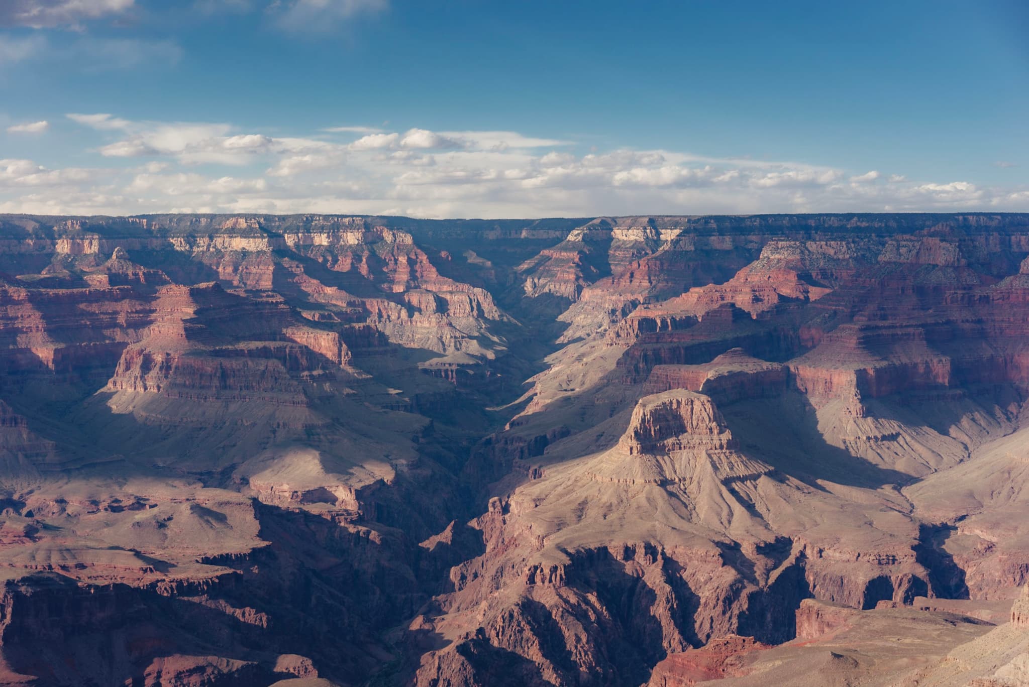 A vast canyon landscape with layered rock formations, deep valleys, and a clear blue sky above