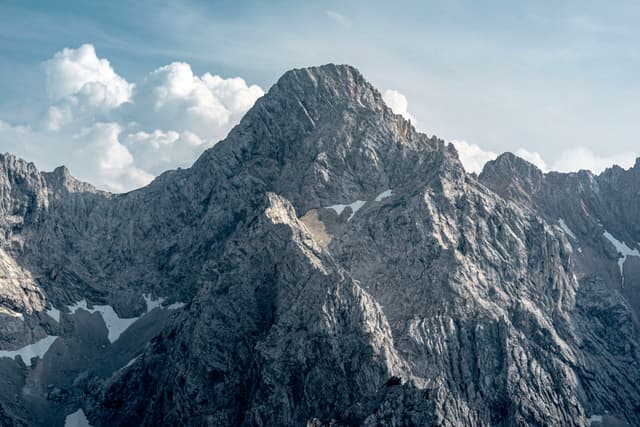 A rugged mountain peak with rocky terrain under a partly cloudy sky