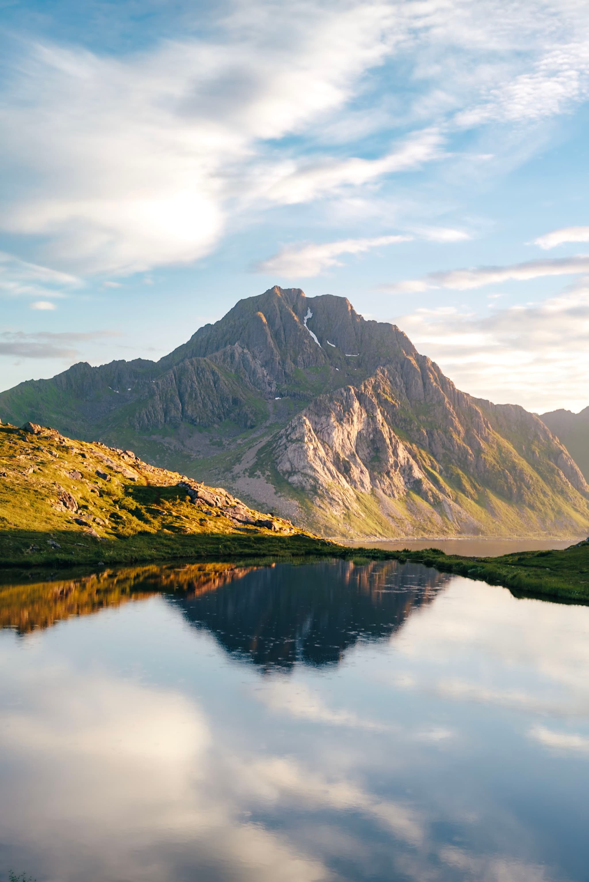 A mountain reflected in a calm body of water, with a clear sky and scattered clouds above