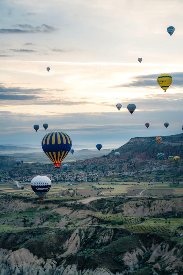 Hot air balloons floating over a scenic landscape with rolling hills and a distant town under a cloudy sky