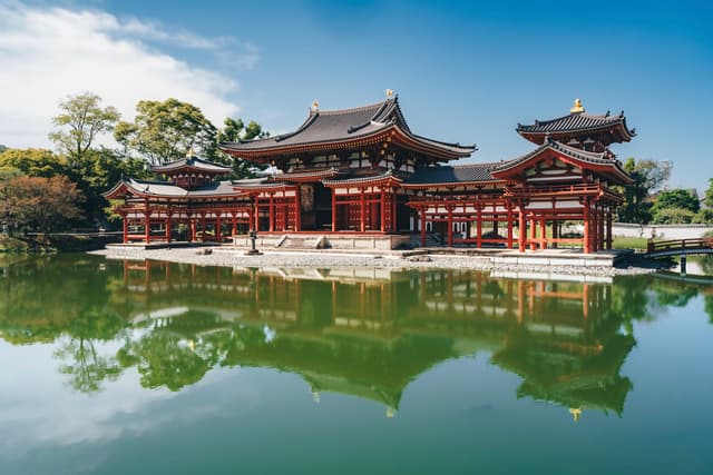 Traditional red temple complex reflected in a calm green pond under a clear blue sky