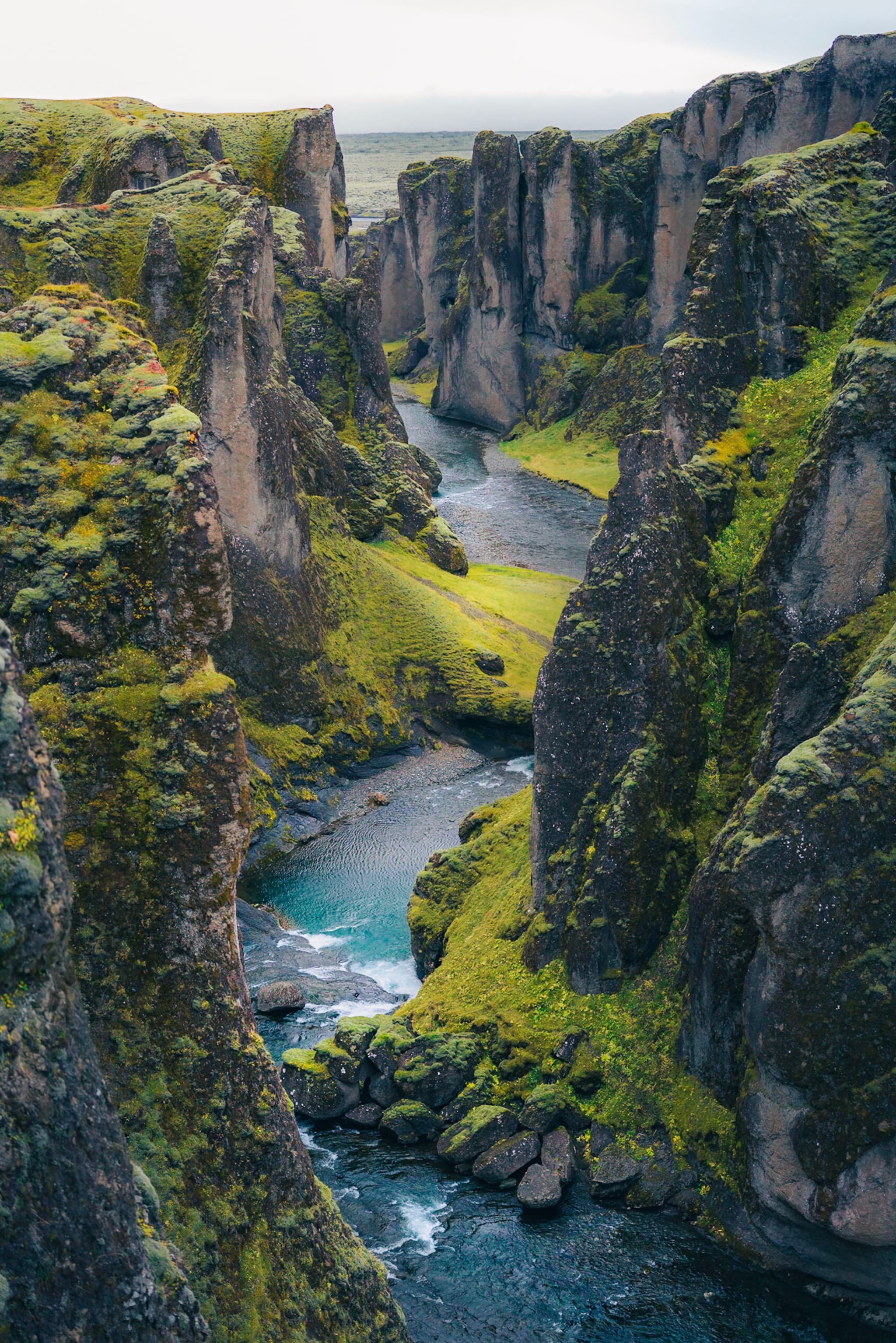 Narrow turquoise river winding between steep moss-covered cliffs in a dramatic green canyon landscape