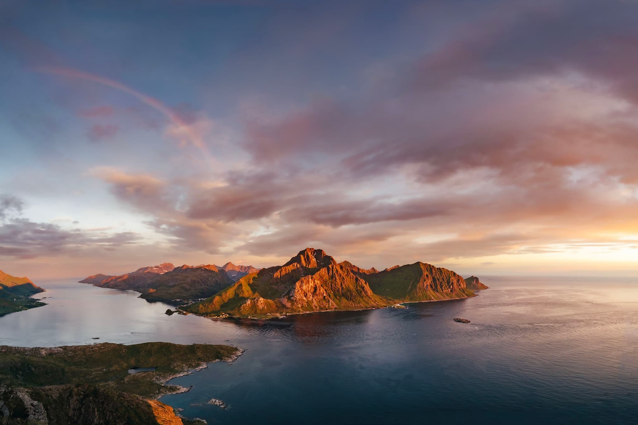 A breathtaking coastal landscape with rugged mountains bathed in warm sunlight, surrounded by calm blue waters under a dramatic sky with scattered clouds