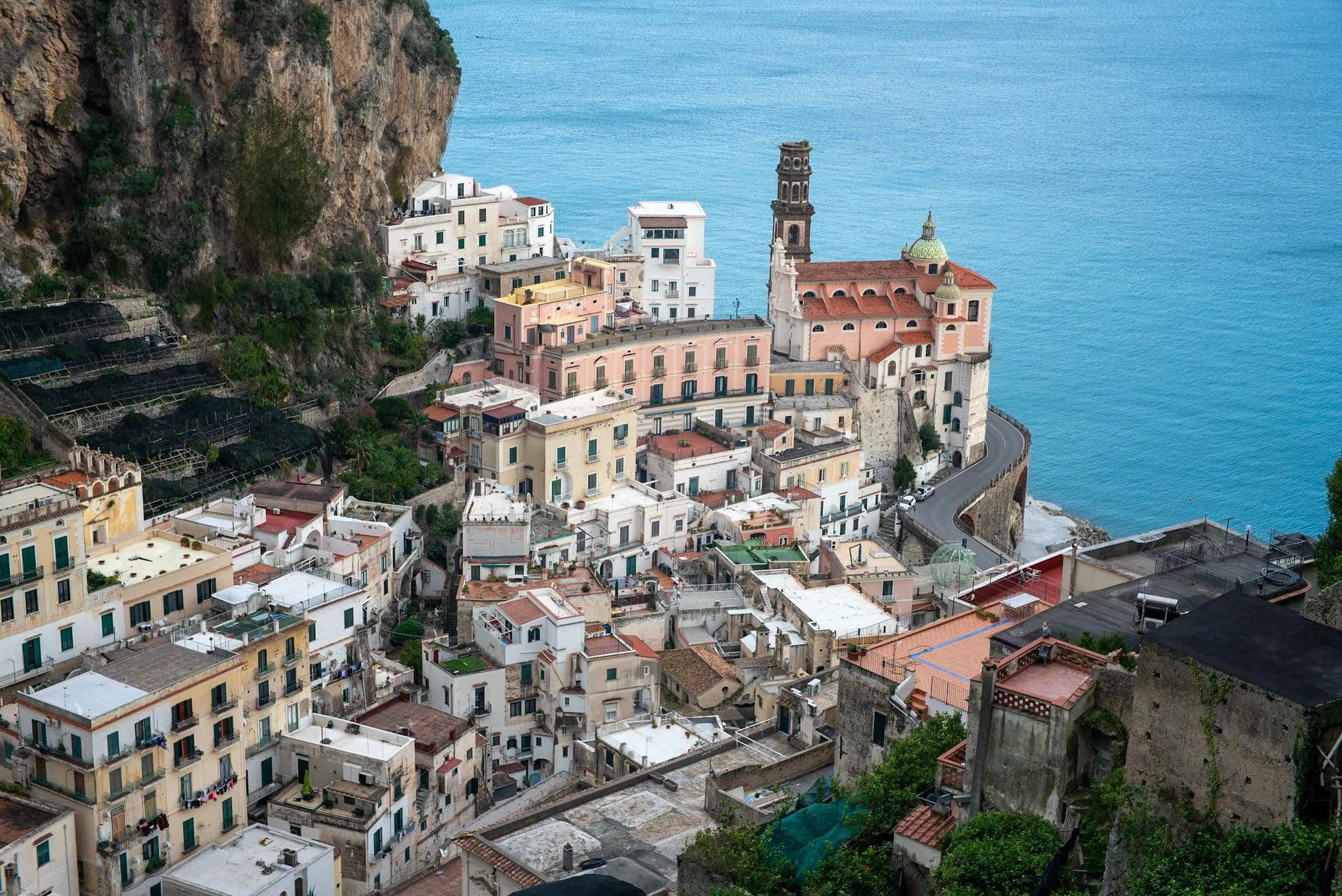 Colorful hillside village built against steep cliffs beside a calm blue sea, with clustered buildings, a church tower, and narrow winding streets