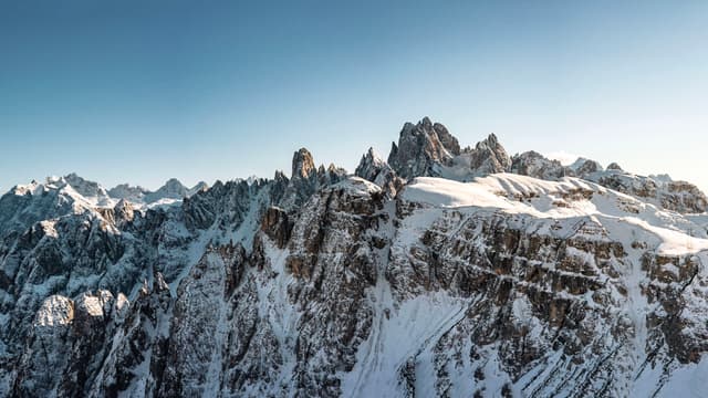 jagged snow-covered mountain range under clear blue sky with sunlight illuminating sharp ridgeline peaks