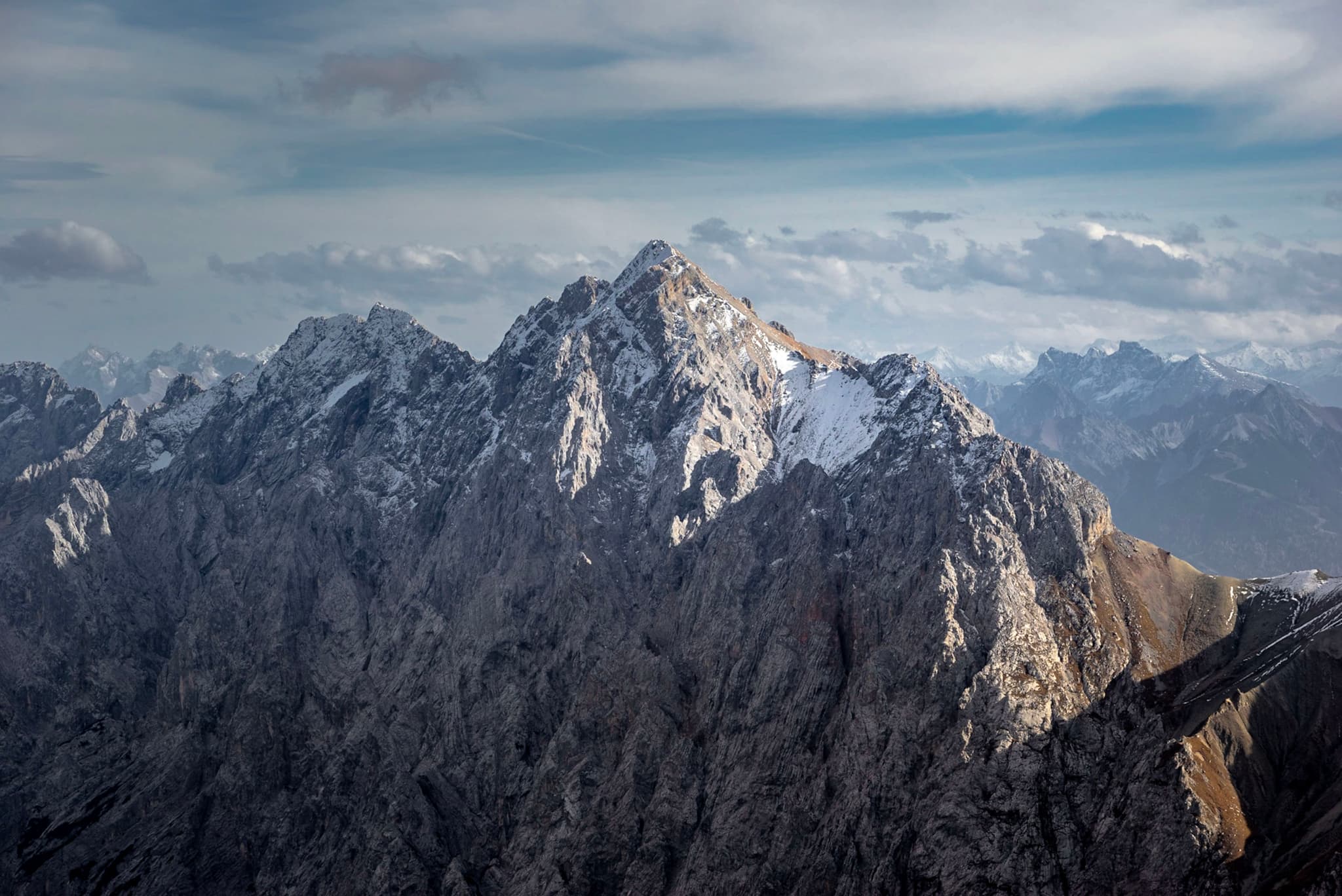 Rugged, snow-dusted mountain peaks rising sharply under a partly cloudy sky