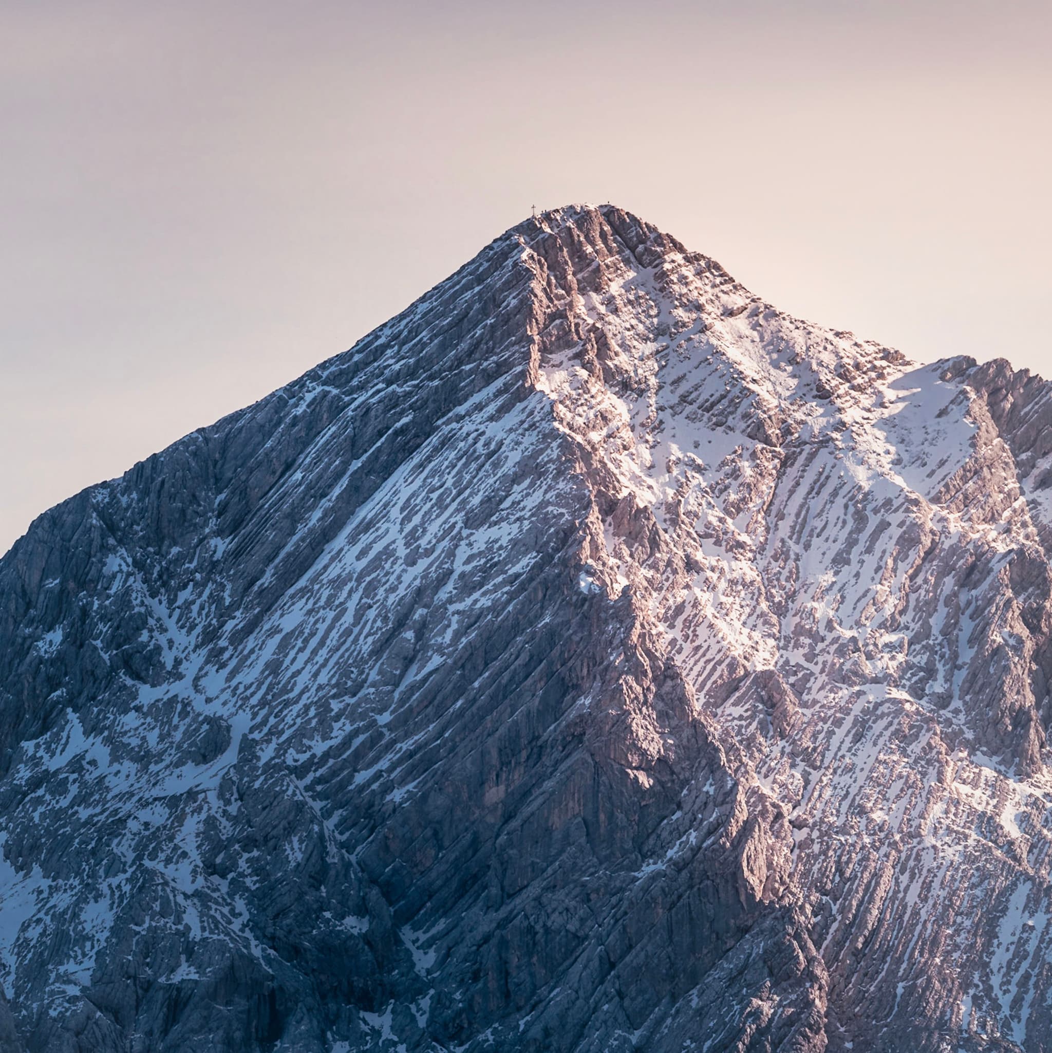 Snow-dusted mountain peak glowing with soft pink light against a pale sky