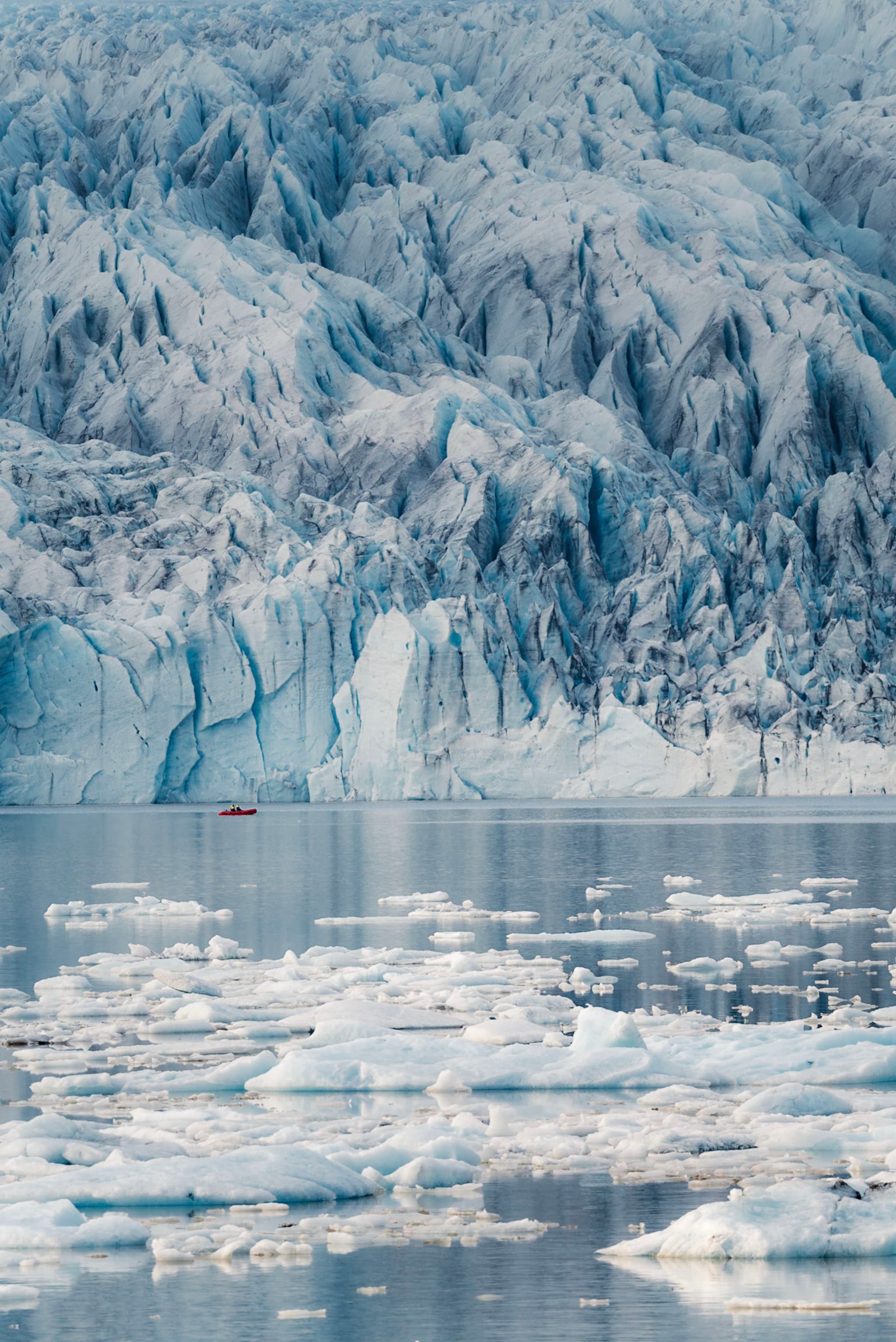 Towering glacier face above calm water dotted with floating icebergs