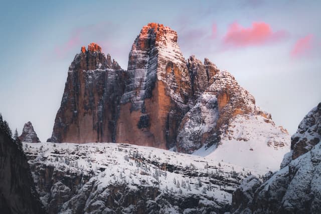 towering snow-covered mountain peaks glowing with warm light under a pastel pink and blue sky