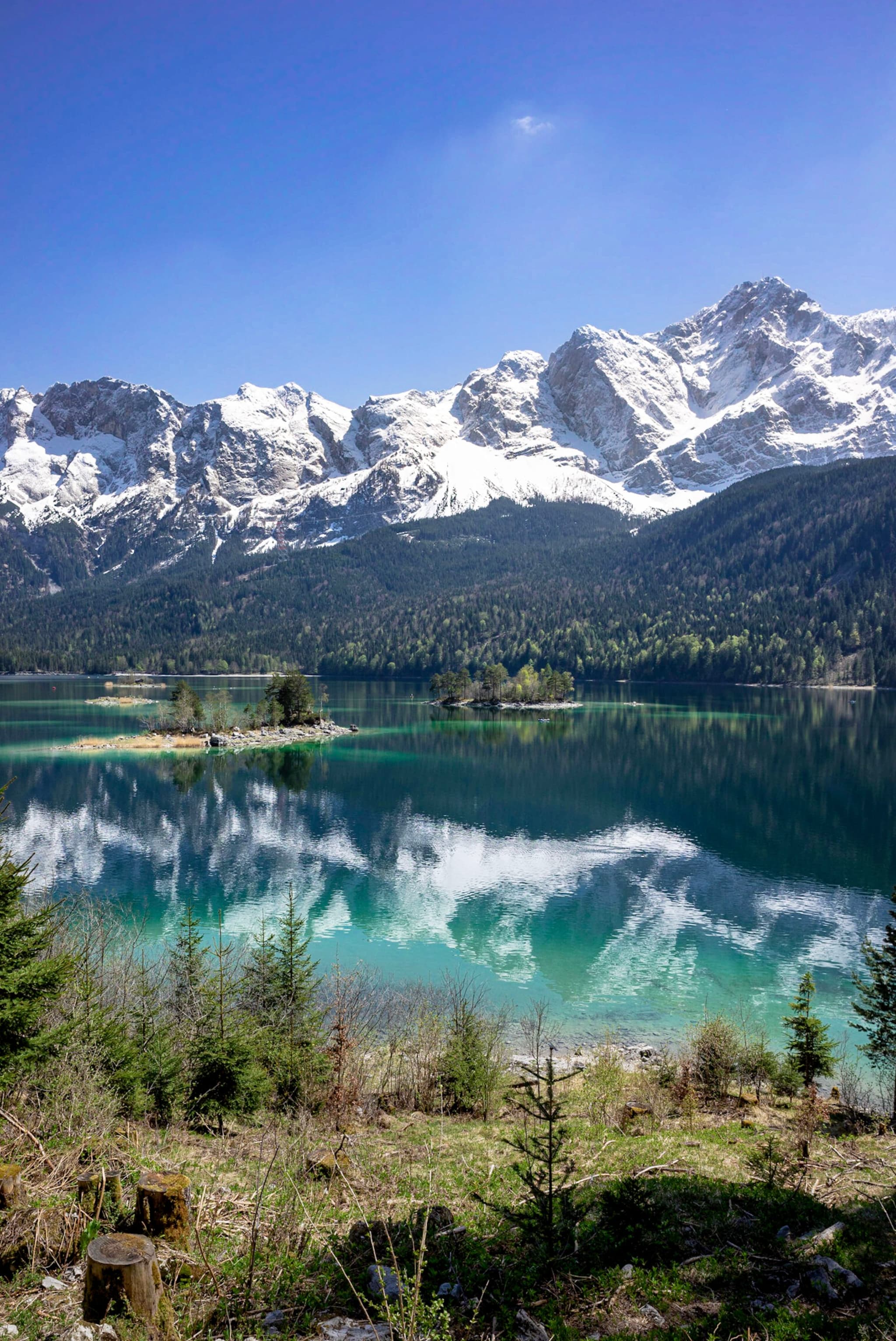 Turquoise alpine lake reflecting snow-covered mountain peaks and surrounding conifer forest under a clear blue sky